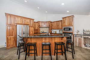 Kitchen with a breakfast bar, a kitchen island with sink, stainless steel appliances, decorative backsplash, and dark stone counters