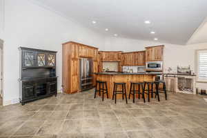 Kitchen with a breakfast bar area, high vaulted ceiling, appliances with stainless steel finishes, an island with sink, and backsplash