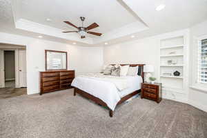 Bedroom with crown molding, a tray ceiling, ceiling fan, and carpet flooring