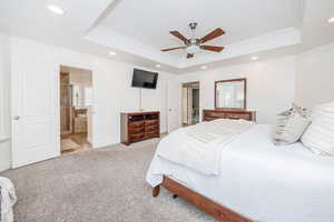 Bedroom featuring connected bathroom, crown molding, light colored carpet, a tray ceiling, and ceiling fan