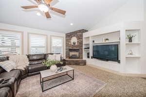 Living room featuring vaulted ceiling, a fireplace, carpet floors, ceiling fan, and built in shelves