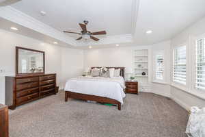 Bedroom with ceiling fan, ornamental molding, a raised ceiling, and carpet