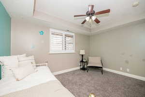 Carpeted bedroom with a textured ceiling, a raised ceiling, and ceiling fan