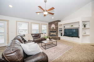 Living room featuring a fireplace, built in shelves, vaulted ceiling, and carpet