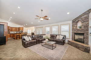 Living room featuring ceiling fan, a fireplace, and vaulted ceiling