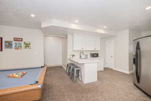 Kitchen with stainless steel fridge, a breakfast bar, white cabinetry, a textured ceiling, and kitchen peninsula