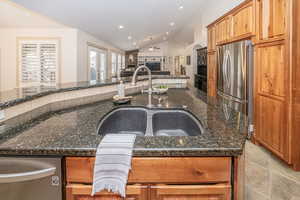 Kitchen with sink, stainless steel refrigerator, vaulted ceiling, dark stone counters, and a large island with sink