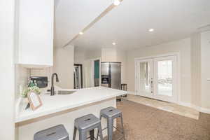 Kitchen with light tile patterned flooring, sink, a breakfast bar area, stainless steel fridge, and kitchen peninsula