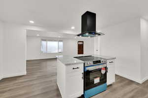 Kitchen with white cabinets, island exhaust hood, light stone countertops, light wood-type flooring, and electric stove