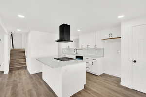 Kitchen featuring black electric stovetop, island range hood, decorative backsplash, and white cabinets