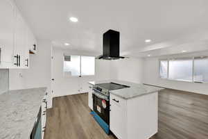 Kitchen with electric stove, island range hood, light stone countertops, white cabinets, and light wood-type flooring