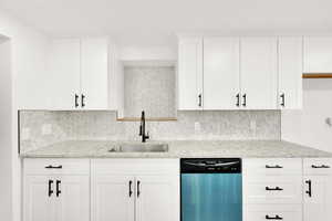 Kitchen with sink, light stone countertops, white cabinets, decorative backsplash, and stainless steel dishwasher