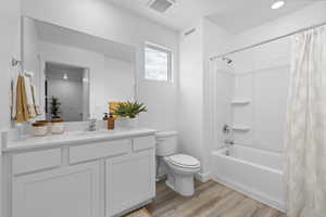 Full bathroom with toilet, wood-type flooring, shower / bathtub combination with curtain, and vanity