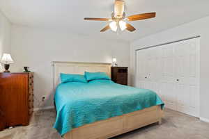 Bedroom with ceiling fan, light colored carpet, and a closet