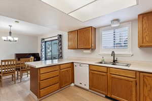 Kitchen with sink, decorative light fixtures, dishwasher, kitchen peninsula, and light hardwood / wood-style floors