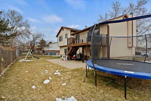 Back of house with a patio area, a trampoline, a yard, a wooden deck, and a playground