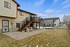 Rear view of property featuring a deck, a lawn, a trampoline, and a patio area