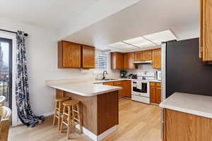 Kitchen with white electric range, stainless steel refrigerator, sink, a kitchen bar, and kitchen peninsula