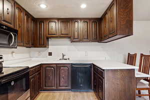 Kitchen with stainless steel electric stove, black dishwasher, sink, and dark brown cabinetry