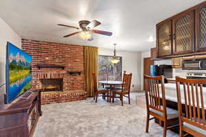 Dining area featuring ceiling fan, a fireplace, light colored carpet, and a textured ceiling