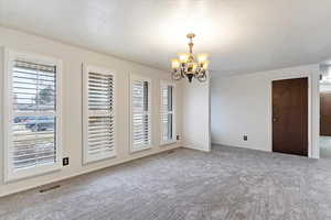 Unfurnished room with carpet flooring, a wealth of natural light, a textured ceiling, and an inviting chandelier