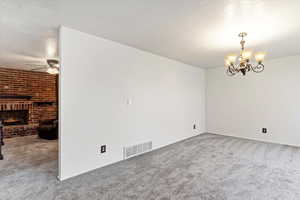 Unfurnished room featuring a brick fireplace, ceiling fan with notable chandelier, carpet, and a textured ceiling