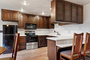 Kitchen featuring sink, a breakfast bar area, dark brown cabinetry, black appliances, and light wood-type flooring