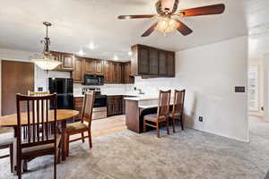 Kitchen featuring stainless steel range with electric stovetop, hanging light fixtures, black refrigerator, light carpet, and kitchen peninsula