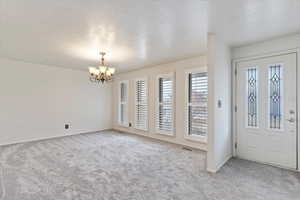 Entryway with a chandelier, light carpet, and a textured ceiling