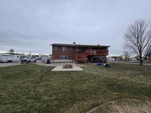 Back of house featuring an outdoor fire pit, a deck, and a lawn