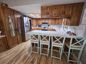 Kitchen with sink, appliances with stainless steel finishes, light hardwood / wood-style floors, a kitchen bar, and kitchen peninsula