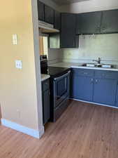 Kitchen with stainless steel range with electric stovetop, under cabinet range hood, a sink, light wood-style floors, and light countertops