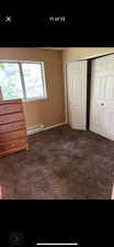 Unfurnished bedroom featuring a baseboard heating unit, a closet, and dark colored carpet