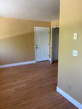 Empty room featuring baseboards, wood finished floors, and a textured ceiling