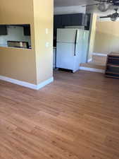 Unfurnished living room featuring ceiling fan, light wood-style flooring, and baseboards