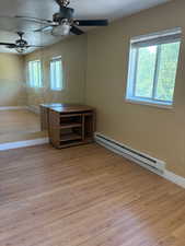 Unfurnished room featuring a baseboard heating unit, a ceiling fan, baseboards, and wood finished floors