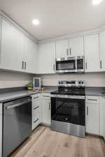 Kitchen with stainless steel appliances, white cabinets, and light hardwood / wood-style floors