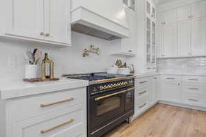 Kitchen with premium range hood, light hardwood / wood-style flooring, double oven range, light stone countertops, and white cabinets