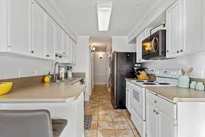 Kitchen with white cabinetry, stainless steel appliances, sink, and light tile patterned floors