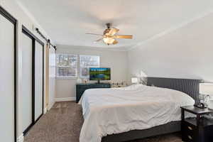 Bedroom featuring crown molding, a barn door, ceiling fan, and carpet