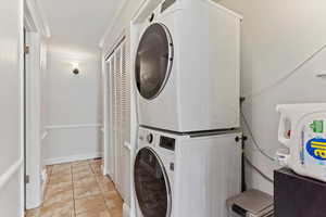 Clothes washing area featuring ornamental molding, stacked washer / drying machine, and light tile patterned floors