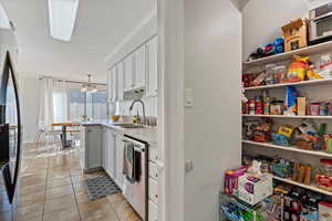 Kitchen with light tile patterned flooring, dishwasher, white cabinetry, sink, and black fridge