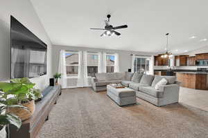 Carpeted living room with sink, ceiling fan with notable chandelier, and vaulted ceiling