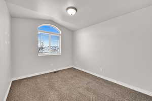 Empty room with vaulted ceiling and carpet