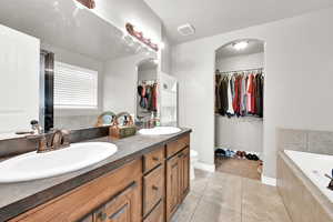 Bathroom featuring tile patterned flooring, vanity, a relaxing tiled tub, and toilet