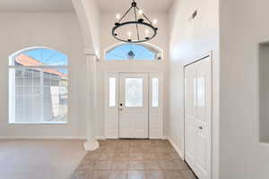 Foyer with a notable chandelier, light tile patterned floors, a high ceiling, and ornate columns