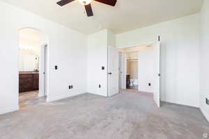 Unfurnished bedroom with ceiling fan, ensuite bath, and light carpet