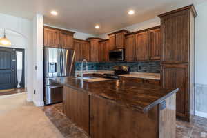 Kitchen featuring an island with sink, sink, decorative backsplash, dark colored carpet, and stainless steel appliances