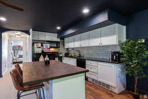 Kitchen featuring wooden counters, black appliances, a center island, and white cabinets