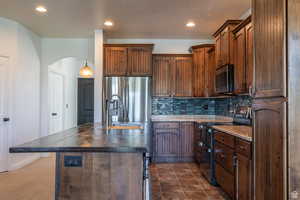 Kitchen with an island with sink, appliances with stainless steel finishes, decorative light fixtures, and decorative backsplash